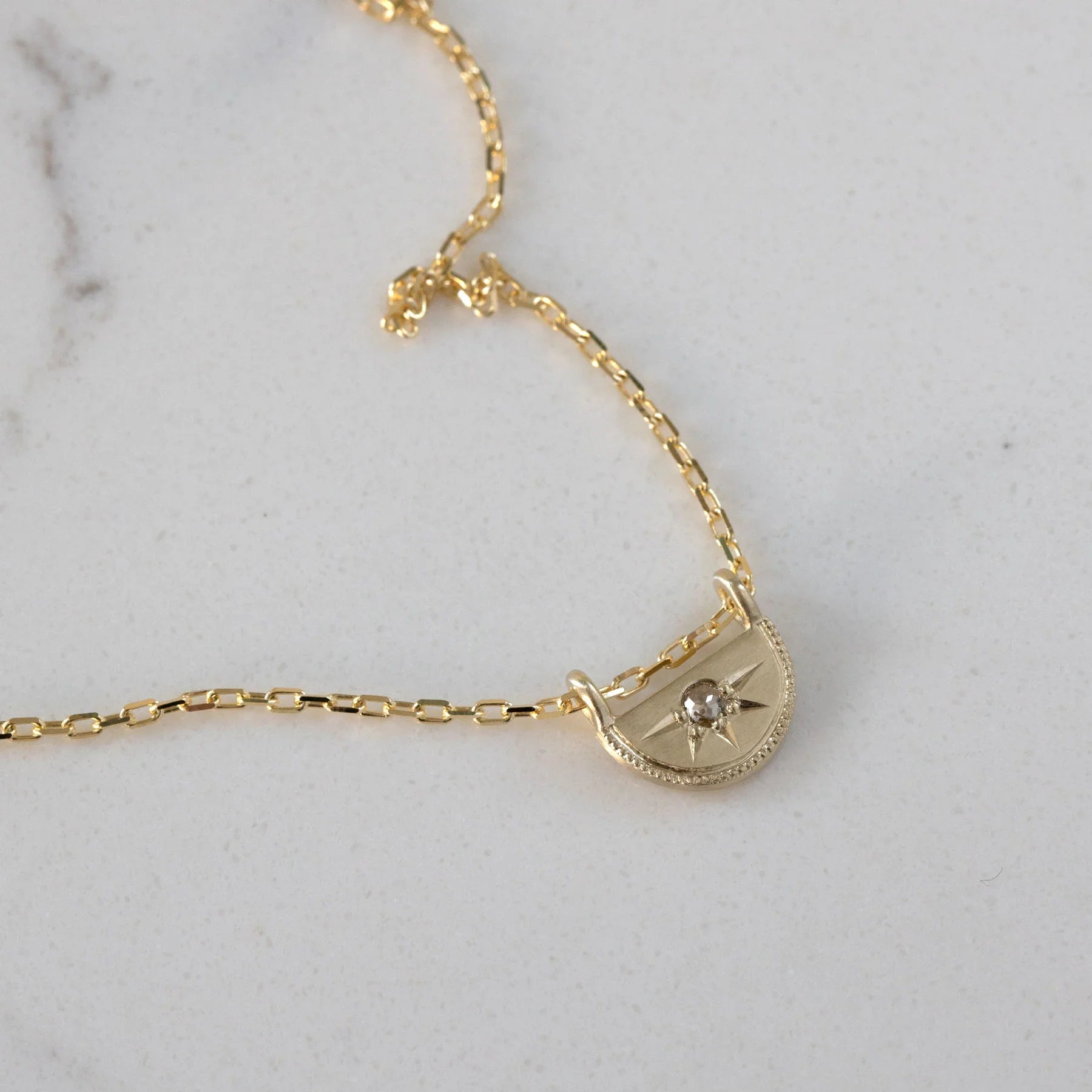 Close-up of handcrafted 14k gold half-moon pendant with rose cut diamond on delicate chain, soft natural light
