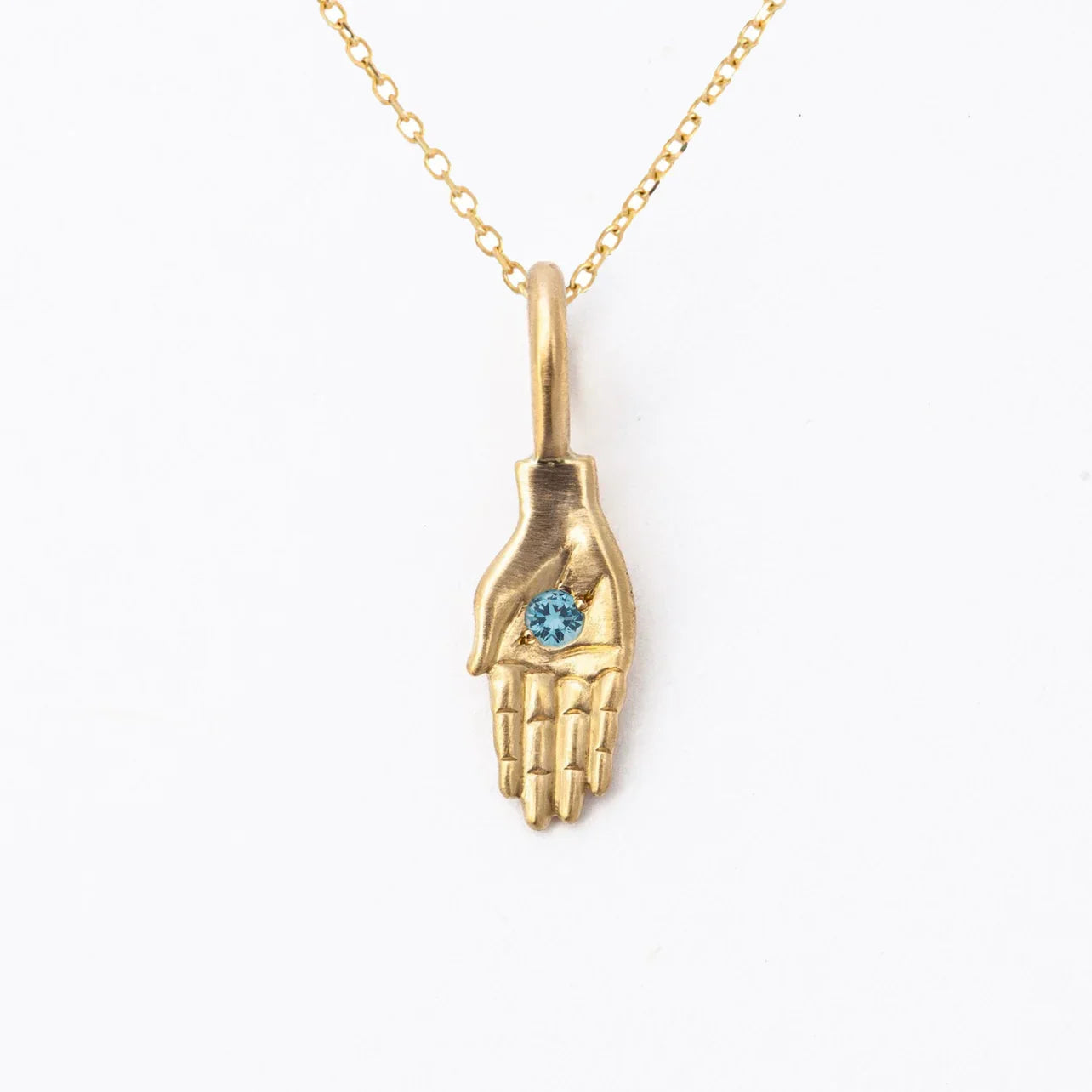 Handcrafted gold hand pendant with blue gemstone on delicate chain, minimalist white background