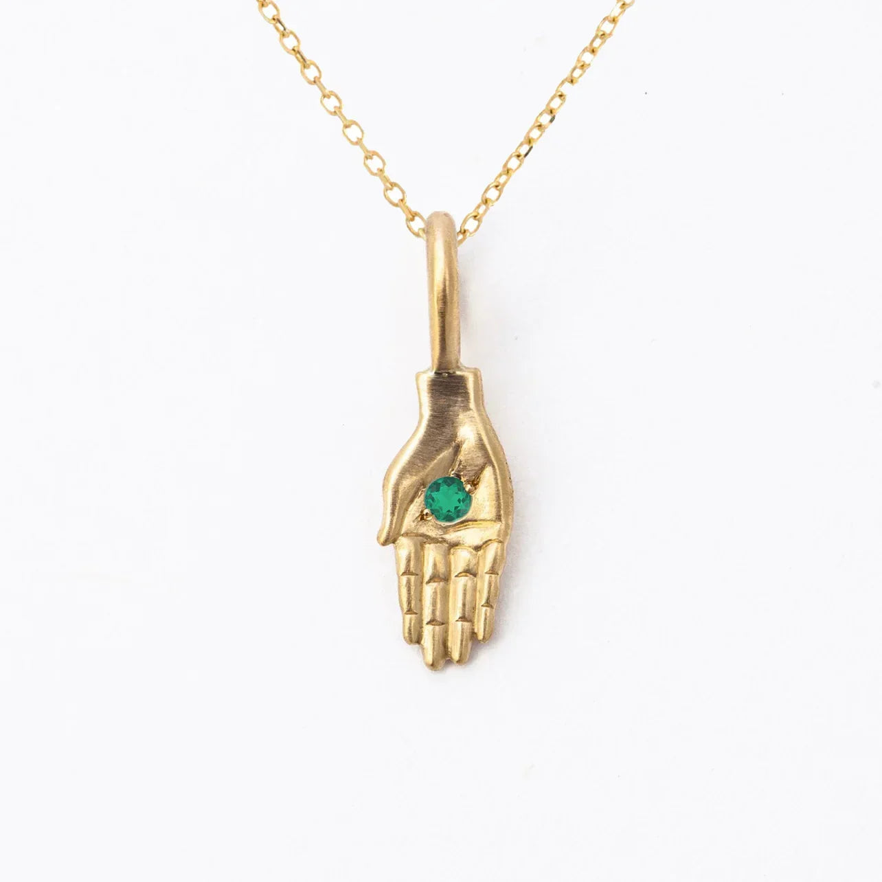 Handcrafted gold pendant shaped as an open hand holding a green gemstone on minimalist white background