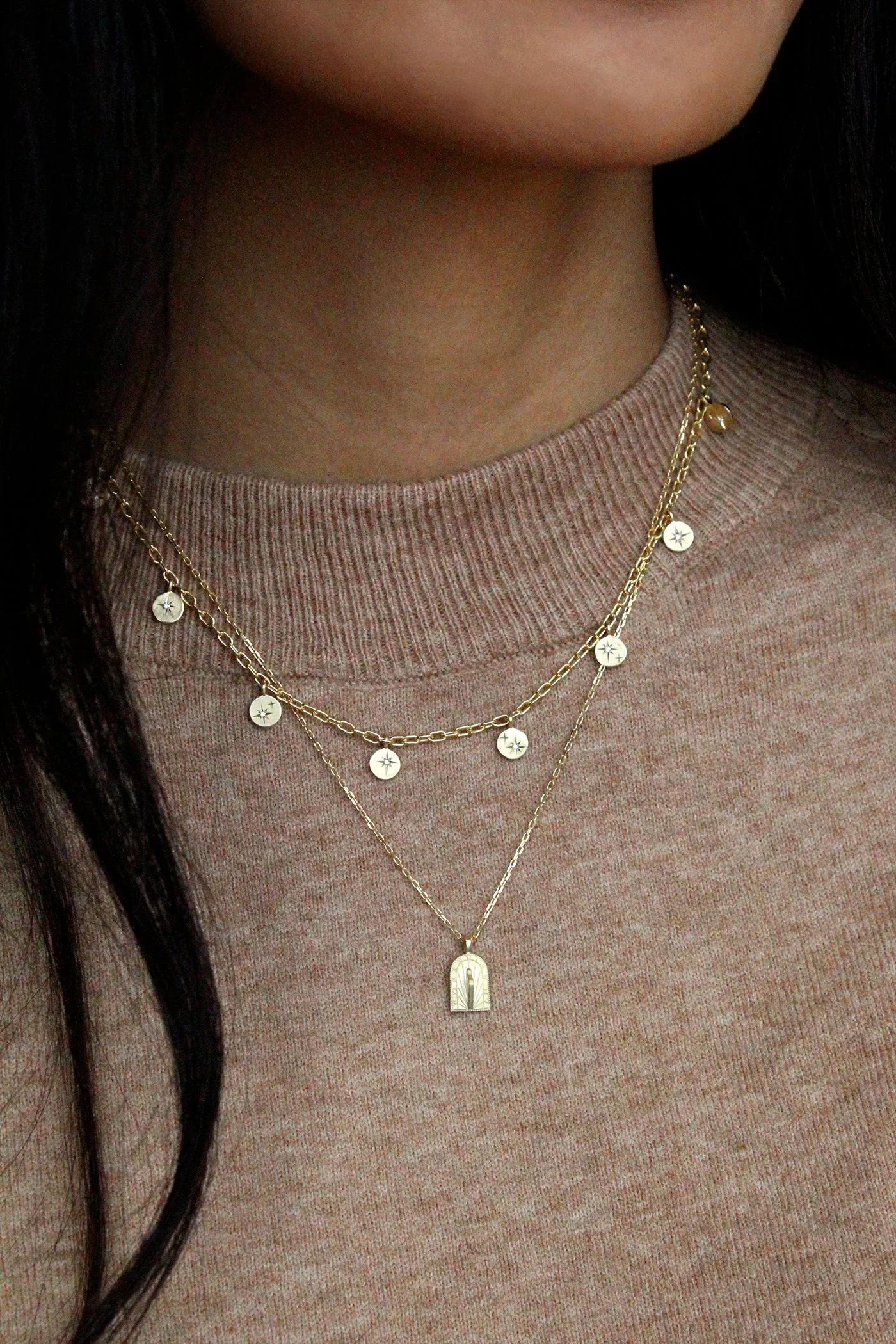 Close-up of layered delicate gold necklaces on beige sweater, featuring star charms and arched pendant