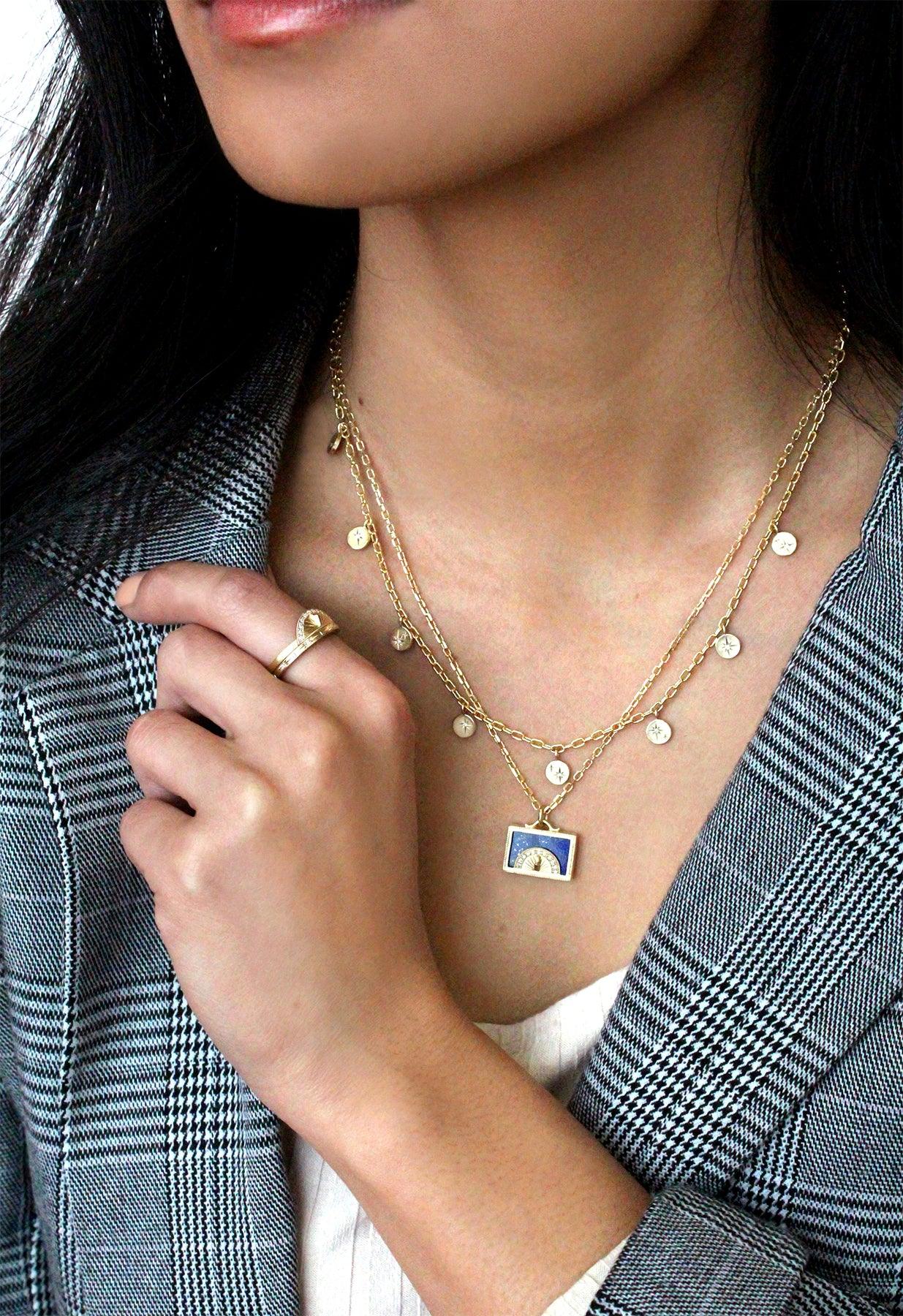 Model wearing layered Fairmined gold necklaces featuring sundial and disc charms with hand-engraved details