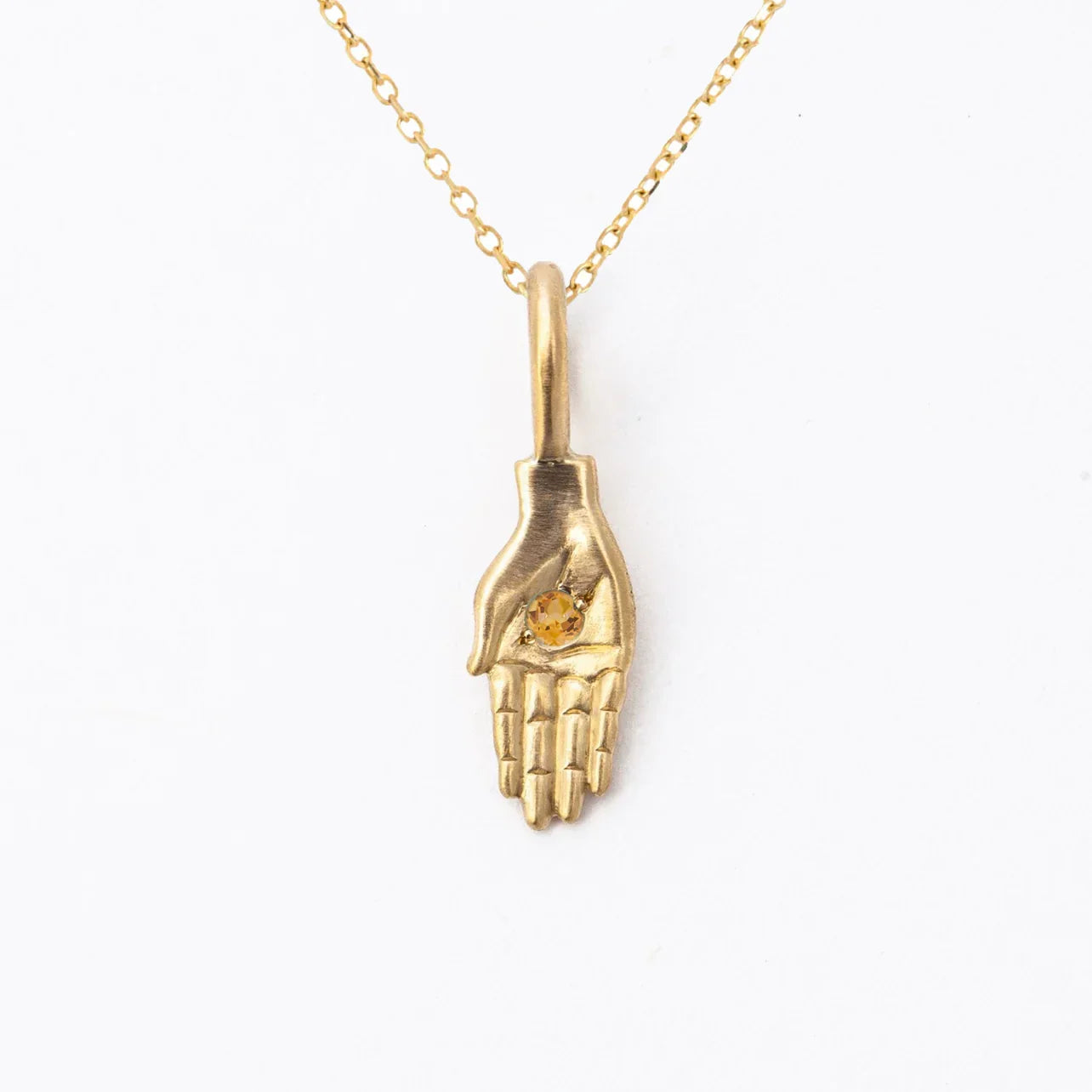 Hand-fabricated gold hand pendant necklace with small citrine gemstone on white background