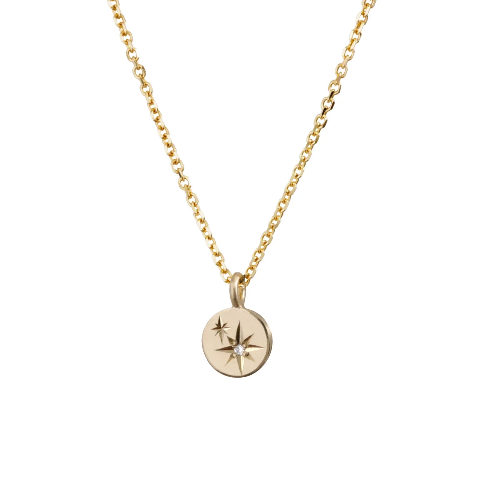 Close-up of hand-fabricated gold pendant necklace with engraved star motifs and center diamond on white background