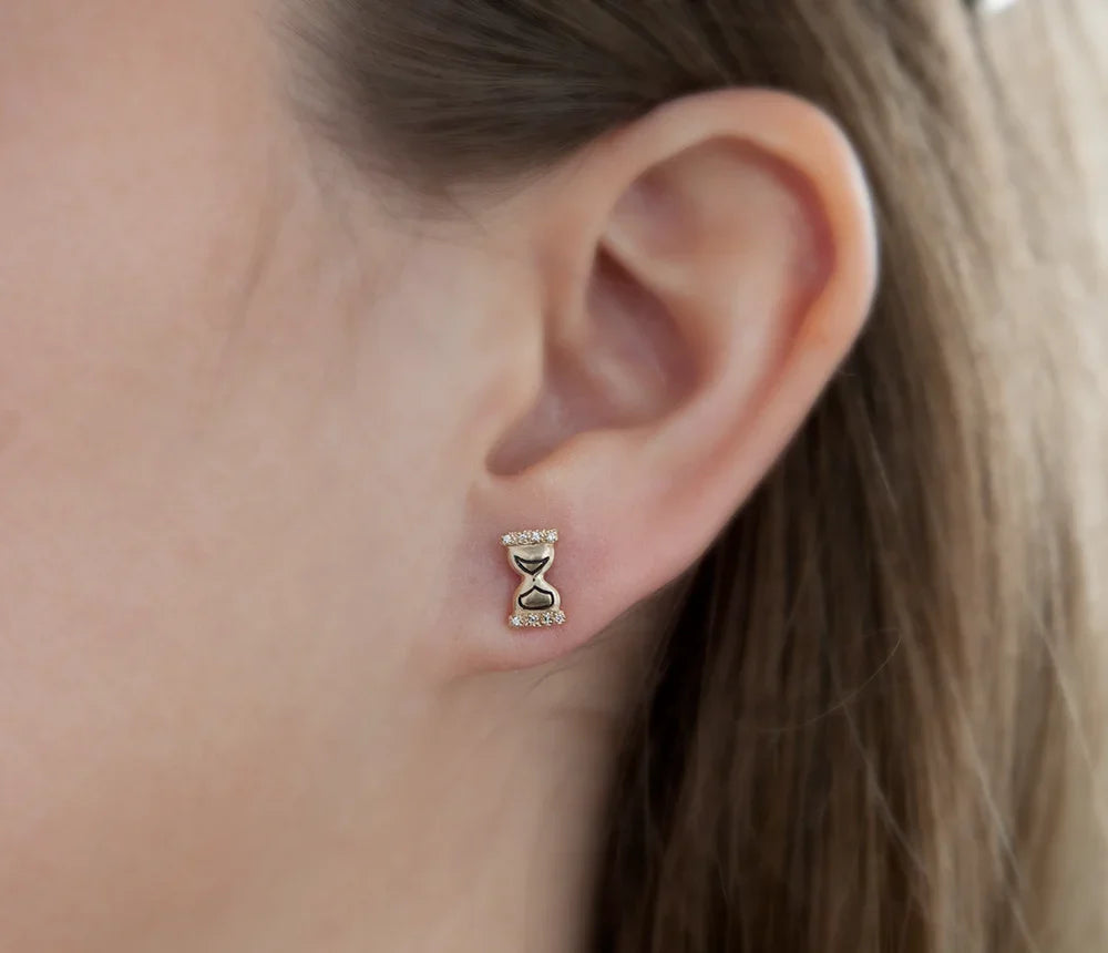 Close-up of gold hourglass stud earring with hand-engraved details worn on ear, soft natural light