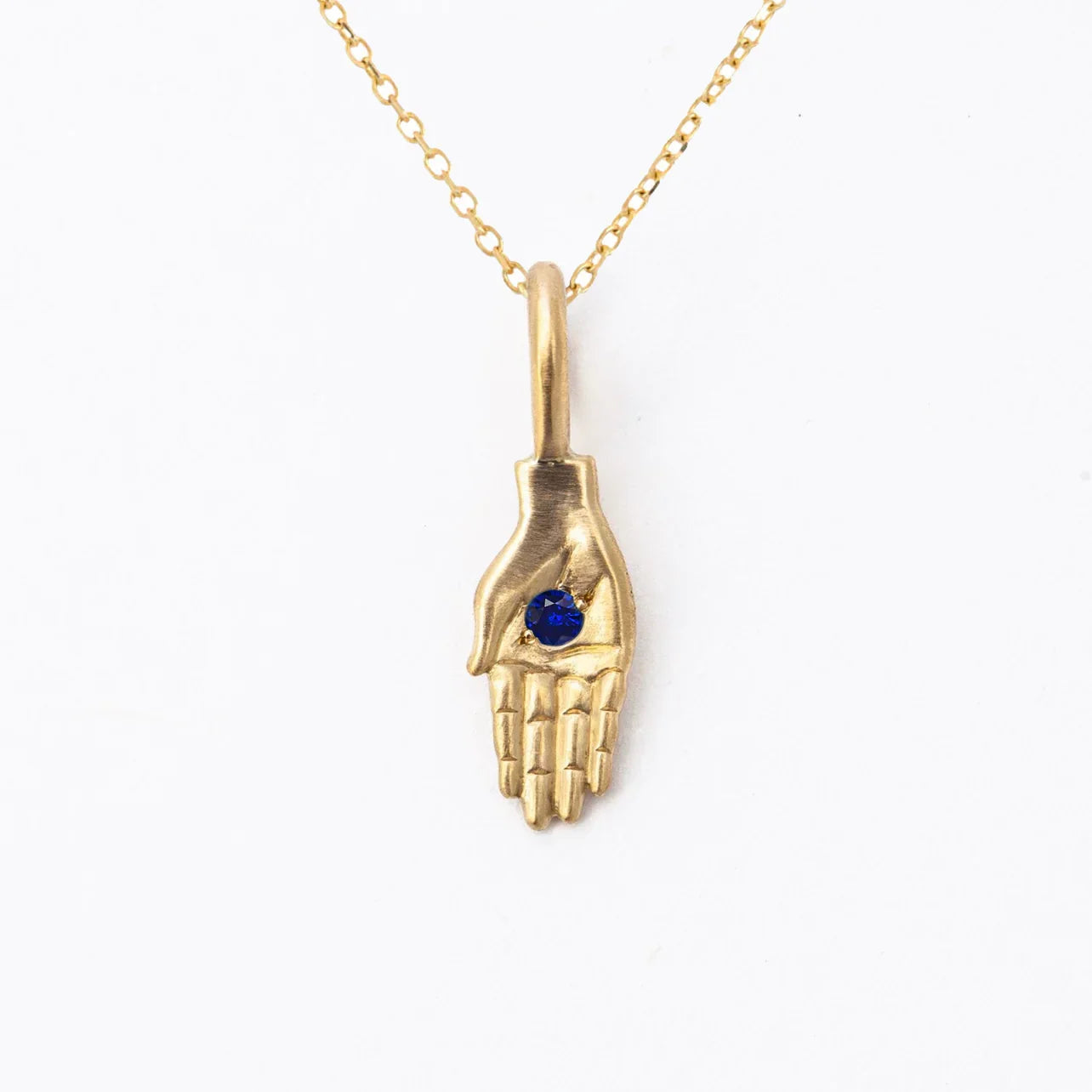 Handcrafted gold hand pendant with deep blue gemstone on delicate gold chain, clean white background