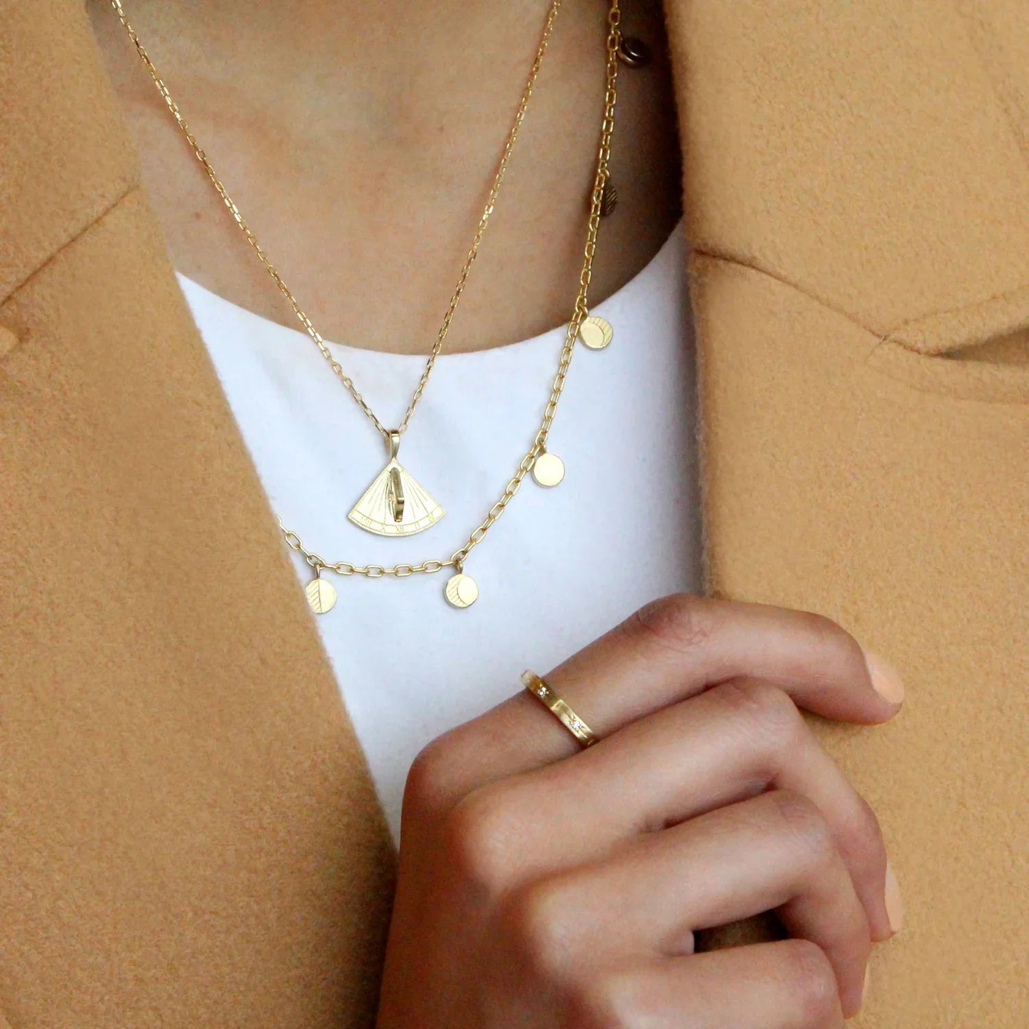 Model wearing layered 14k gold sundial pendant necklace, disc charm chain, and engraved gold ring, warm natural light