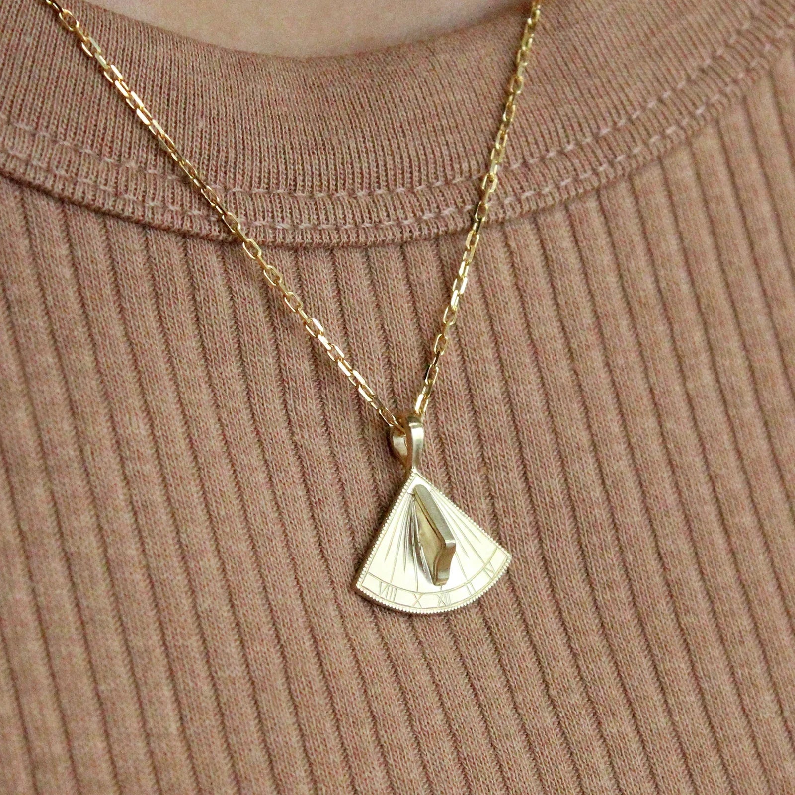 Close-up of 14k gold sundial pendant with functioning gnomon on fine chain, worn over warm beige ribbed knit