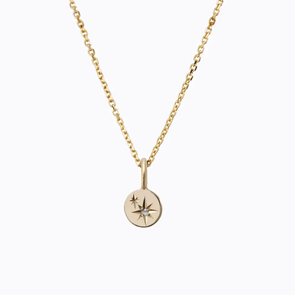 Delicate 14k gold necklace with hand-engraved starburst pendant featuring small seed pearl on white background