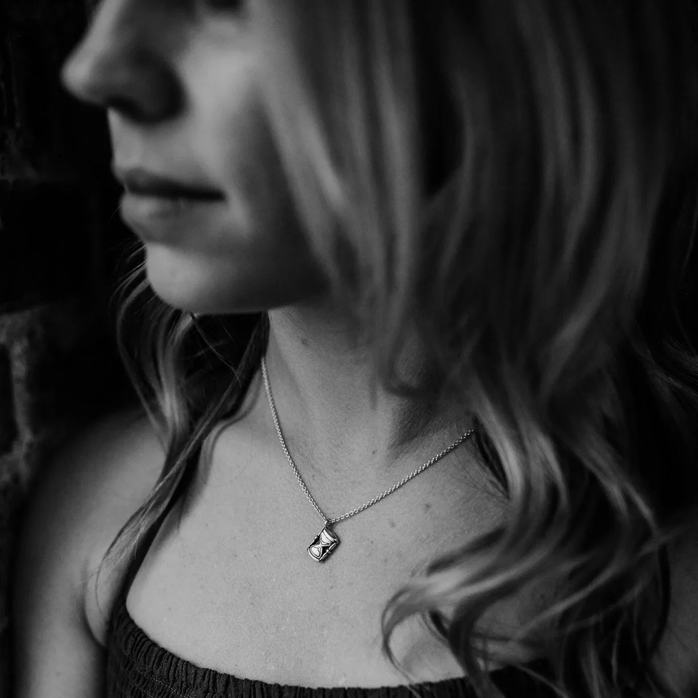 Black and white close-up of woman wearing delicate silver hourglass pendant necklace
