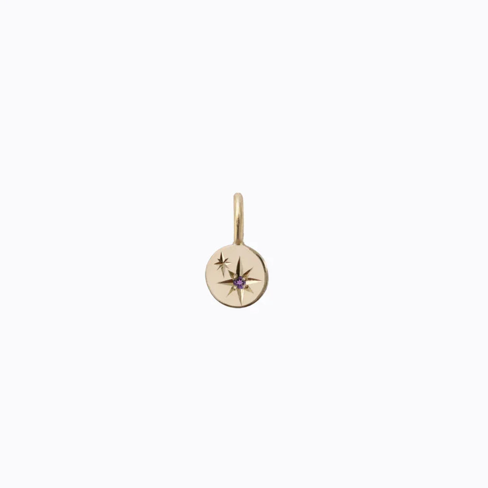 Hand-fabricated gold pendant with engraved star design and small amethyst center on soft white background