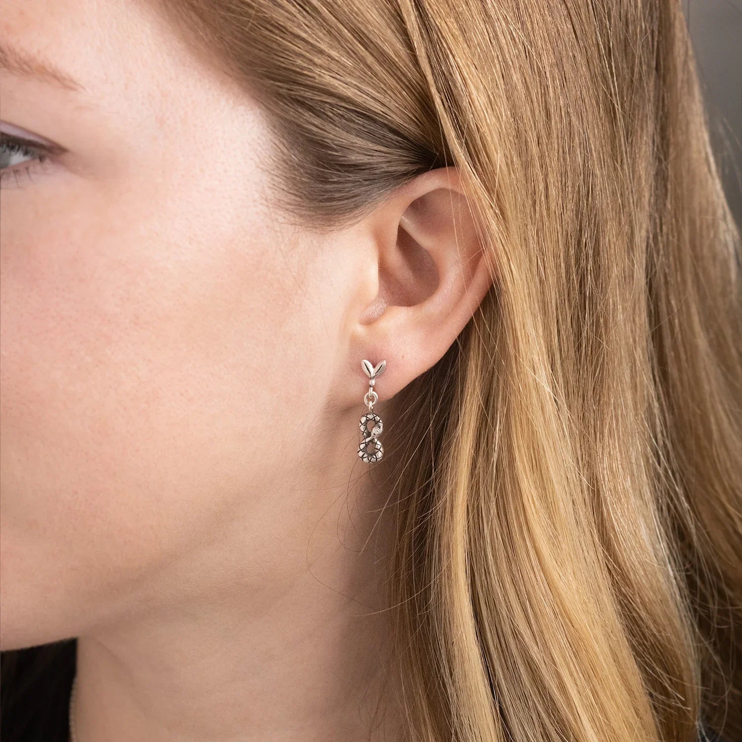 Close-up of delicate silver infinity dangle earring worn by woman with natural light and soft shadows