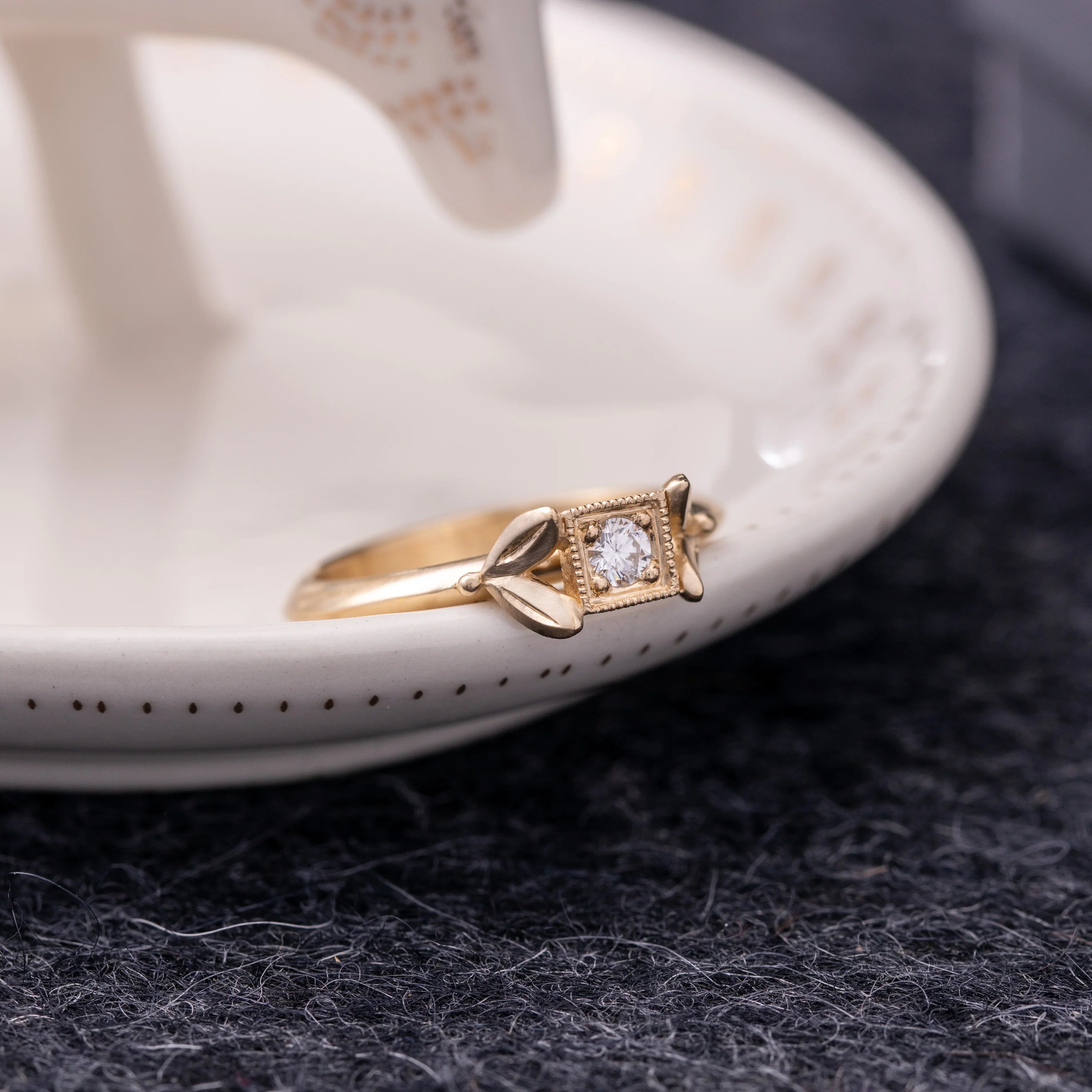 Hand-fabricated gold arrow ring with bezel-set diamond, delicate patina on neutral dish