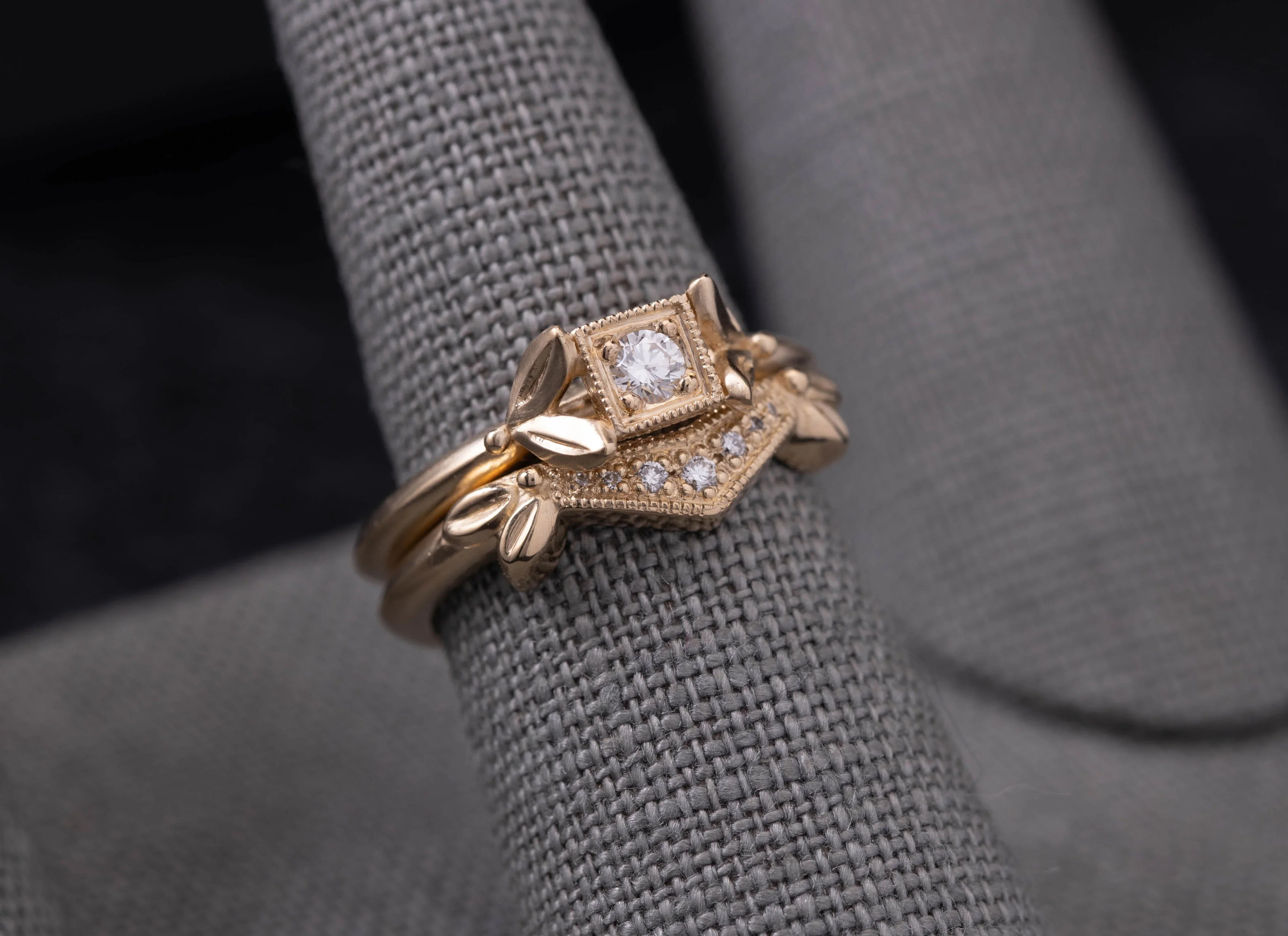 Close-up of delicate gold ring with central diamond and leaf motifs on textured grey fabric
