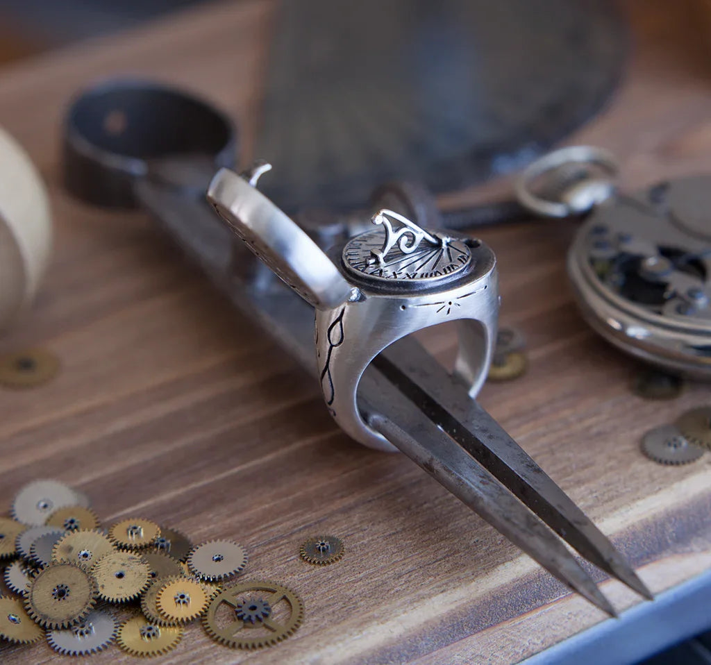Close-up of silver sundial ring with hand-engraved details on antique compass, rustic wooden background