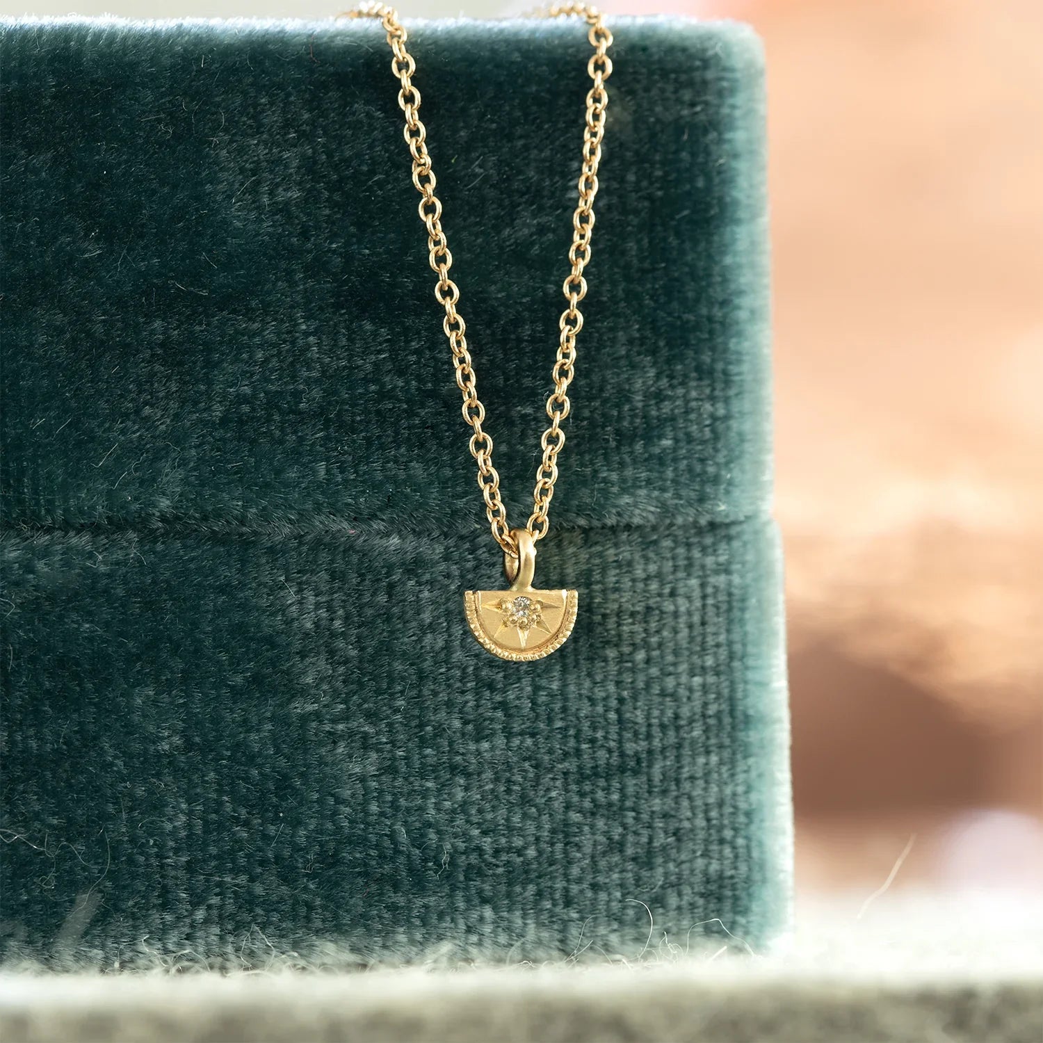 Delicate handcrafted gold sundial pendant with diamond detail on chain, displayed on dark green velvet