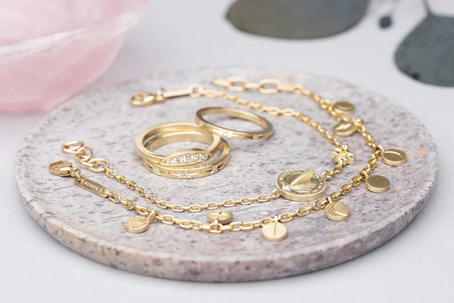 Hand-fabricated gold sundial bracelet and three elegant gold rings on natural stone plate with soft lighting