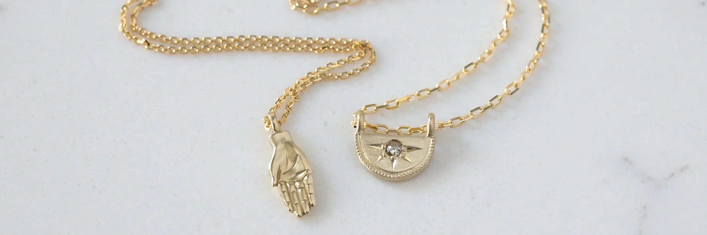 Close-up of two handcrafted gold pendants on delicate chains on a light stone surface