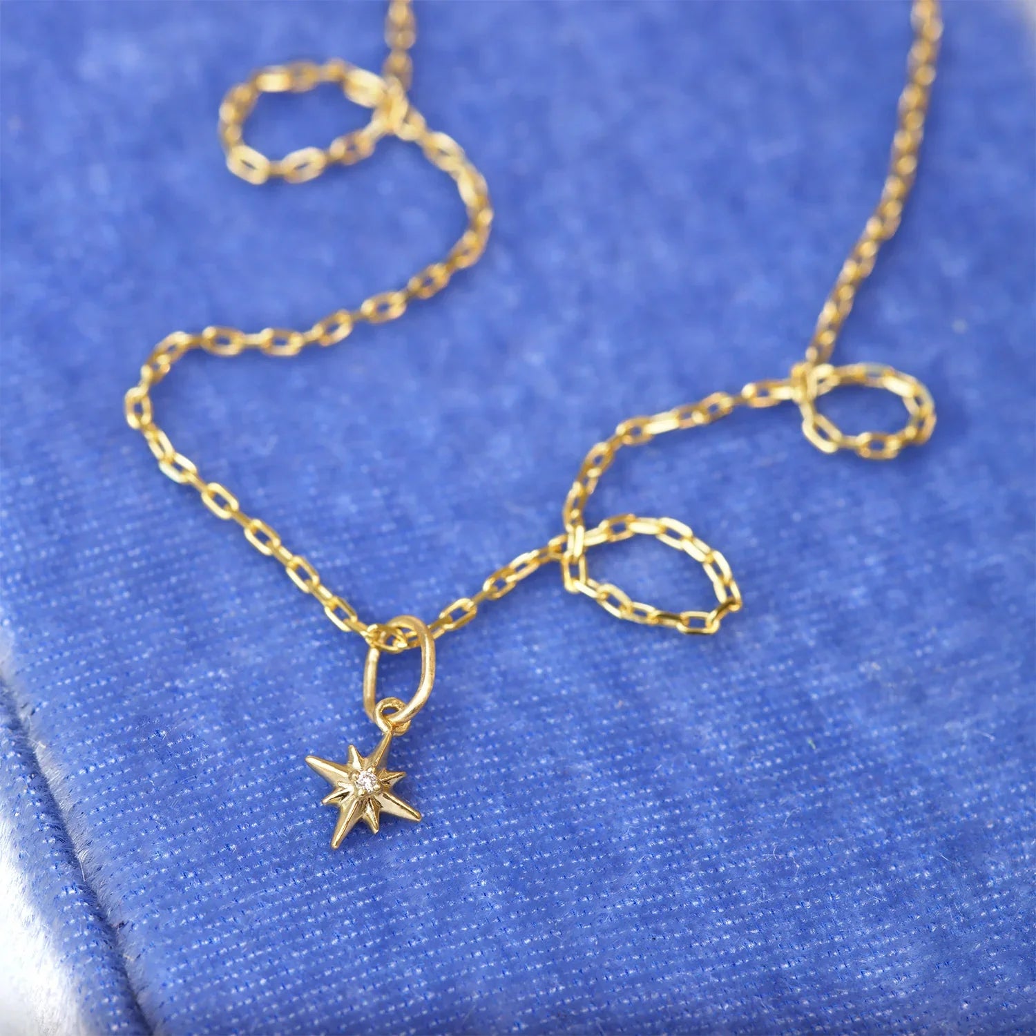 Delicate 10k gold North Star diamond charm necklace on textured blue linen background in warm natural light