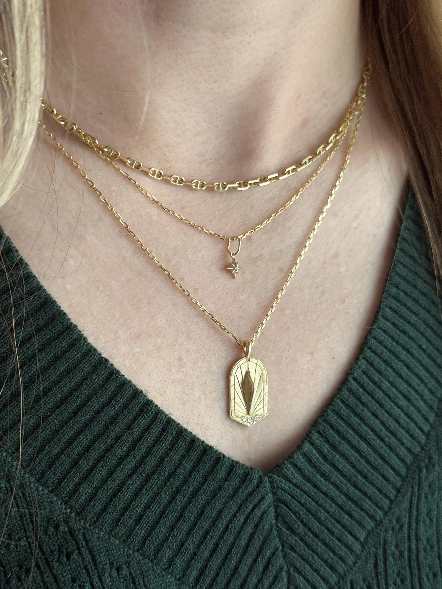 Close-up of layered gold necklaces on woman’s neck featuring delicate star charm and gold sundial pendant in warm natural light